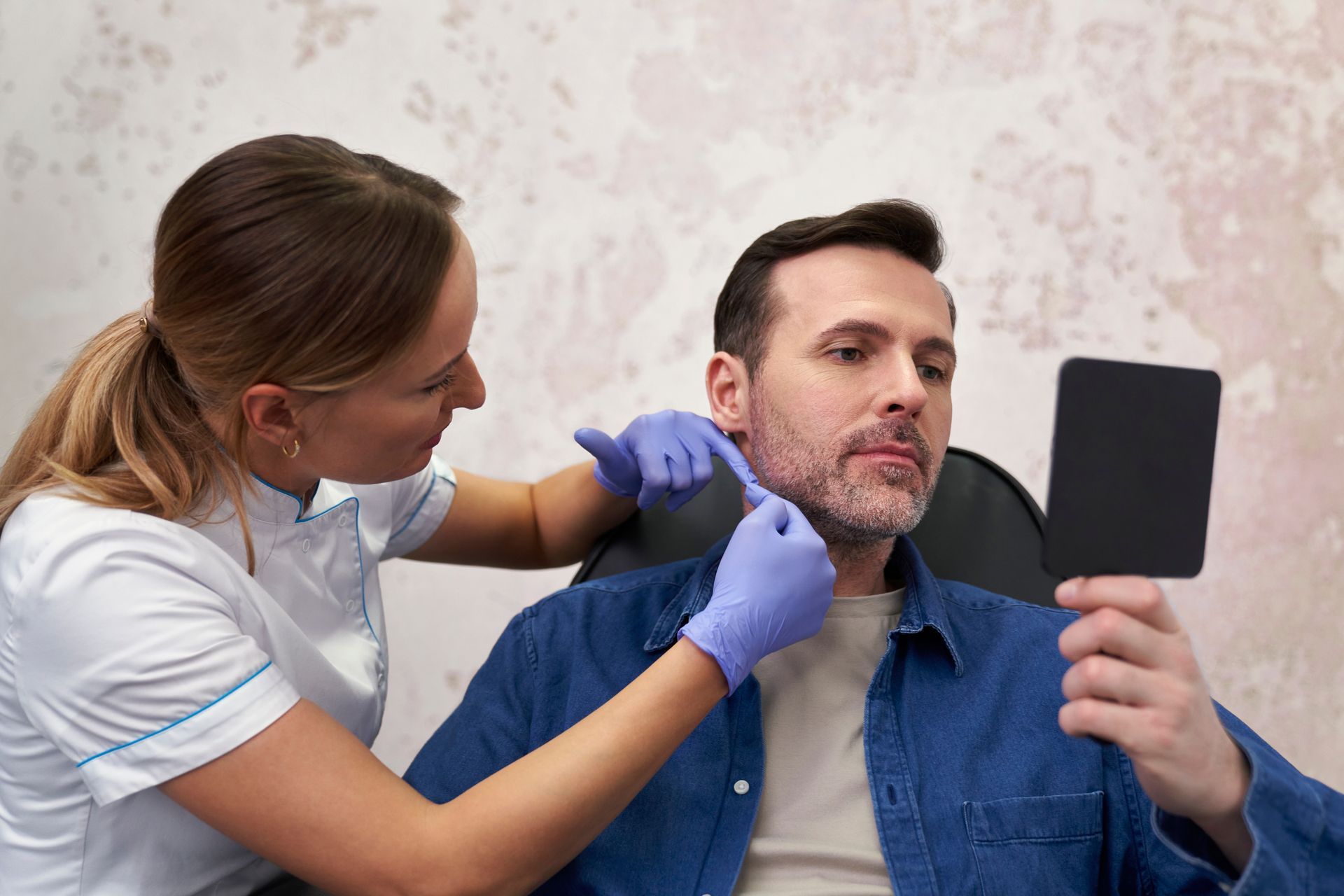 Woman applying makeup to a man holding a mirror in a salon chair