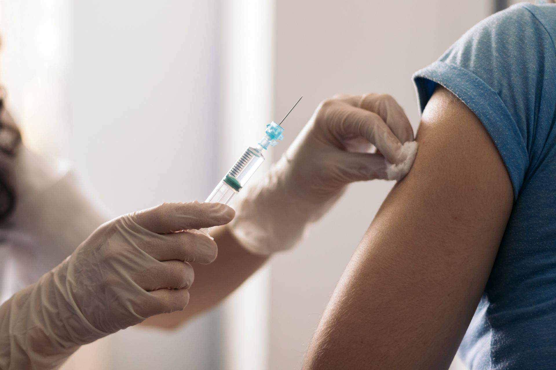 A medical professional administers a vaccine injection in a patient's upper arm. Both wear gloves.