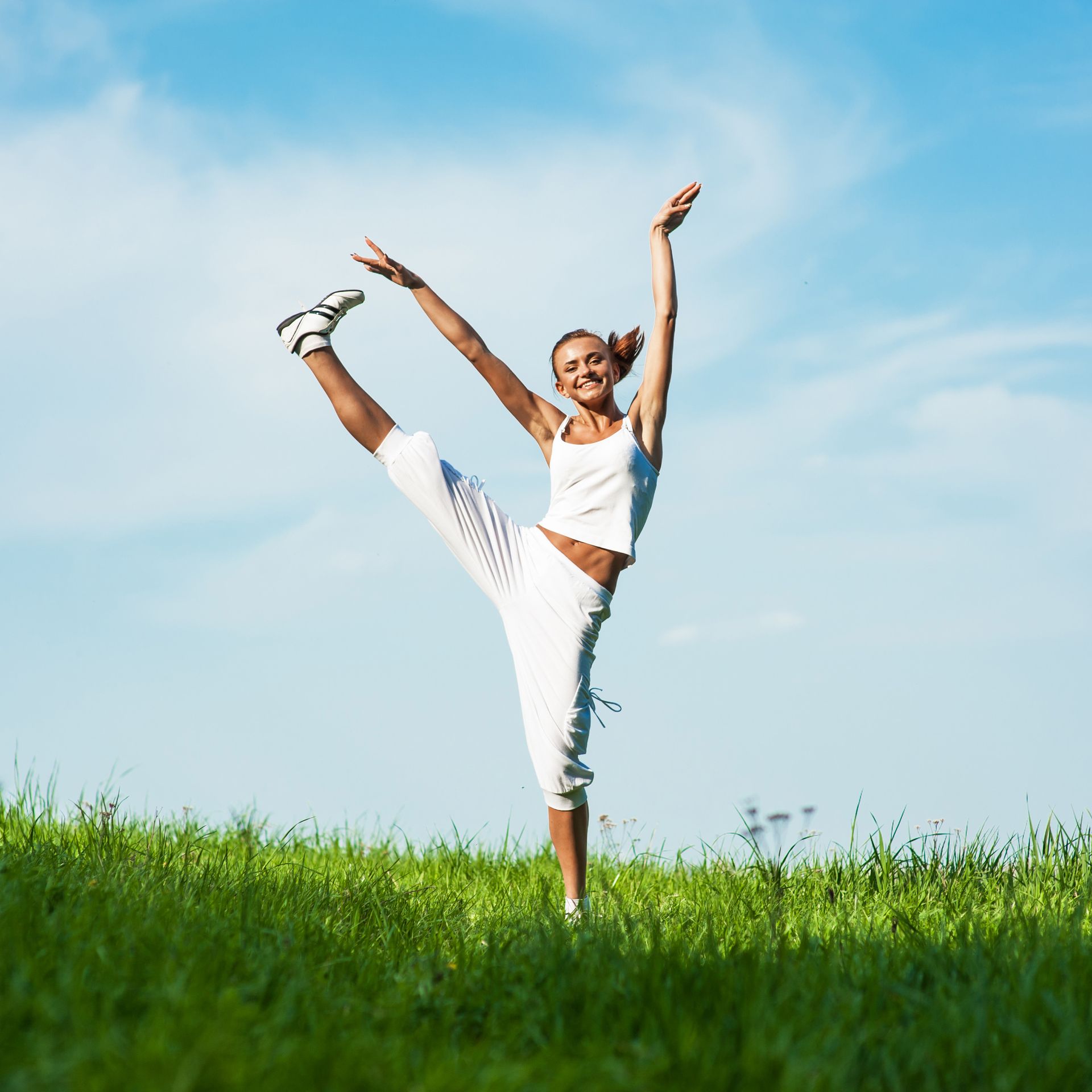 A woman is standing on one leg in a grassy field