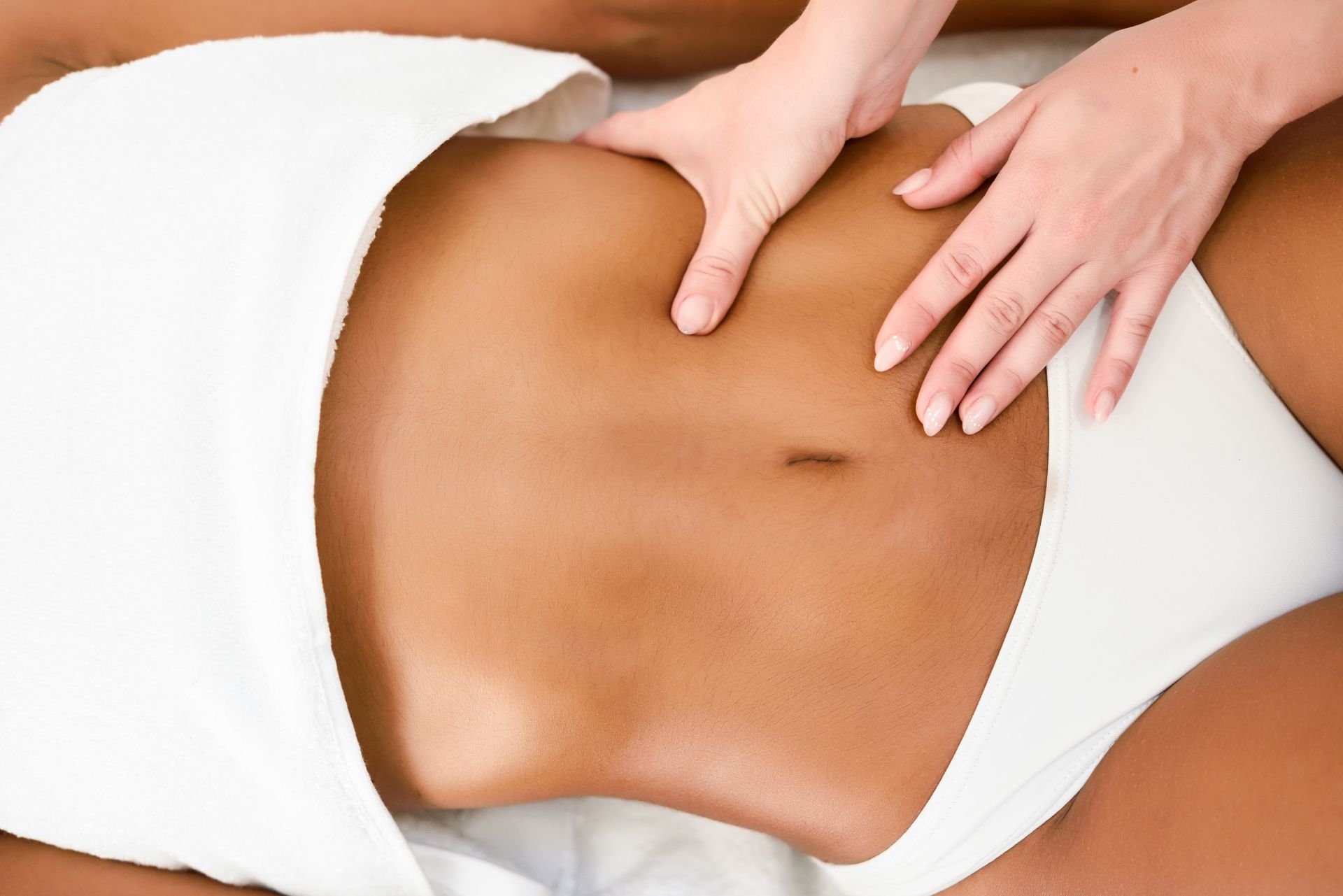 Hands massaging a person's stomach, person is lying down with a white towel covering the lower body.