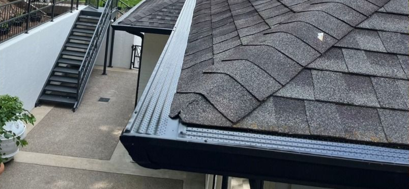 Corner of a house roof with dark soffit and gutters against a blue sky Corner of a house roof with dark soffit and gutters against a blue sky