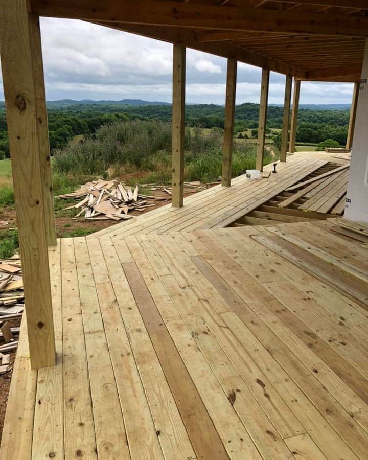 Wooden deck framing with a worker’s boots stepping across exposed beams outdoors Wooden deck framing with a worker’s boots stepping across exposed beams outdoors
