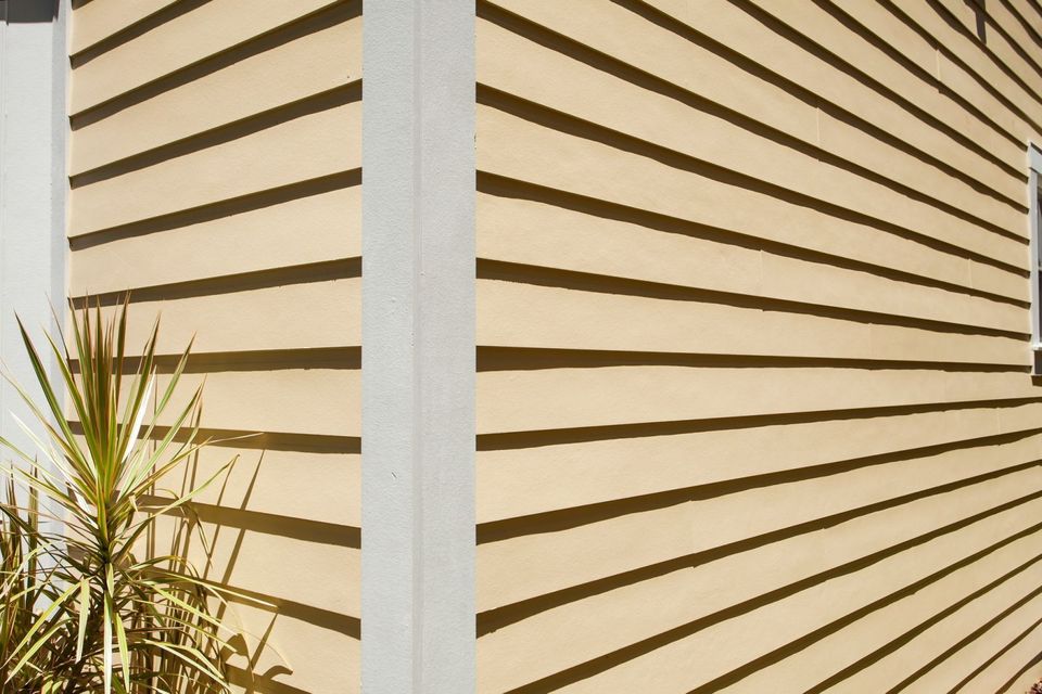 Blue-gray house siding with a white-trimmed window and roof eave viewed from below Blue-gray house siding with a white-trimmed window and roof eave viewed from below