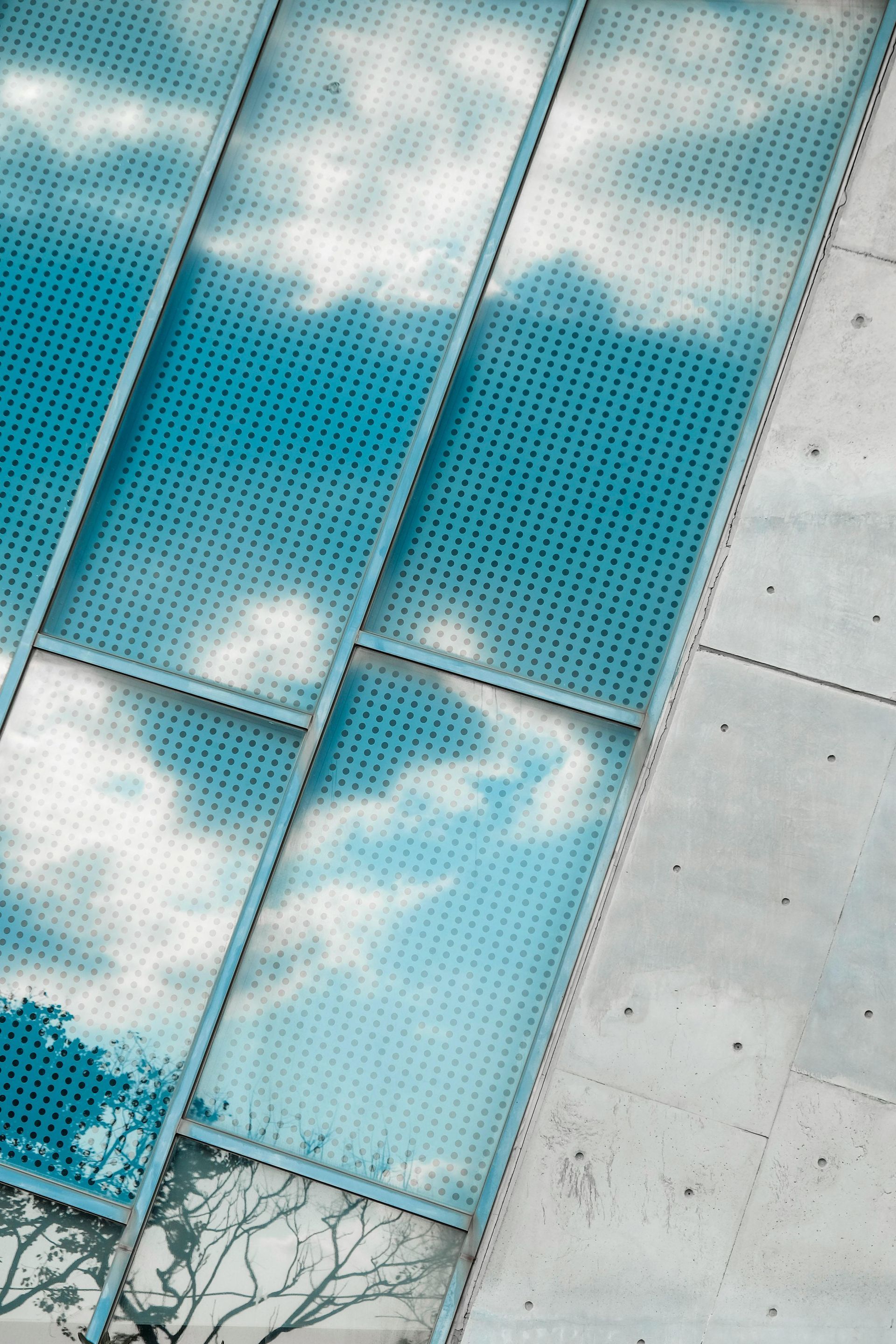An aerial view of a building with a blue sky and clouds reflected in the windows.