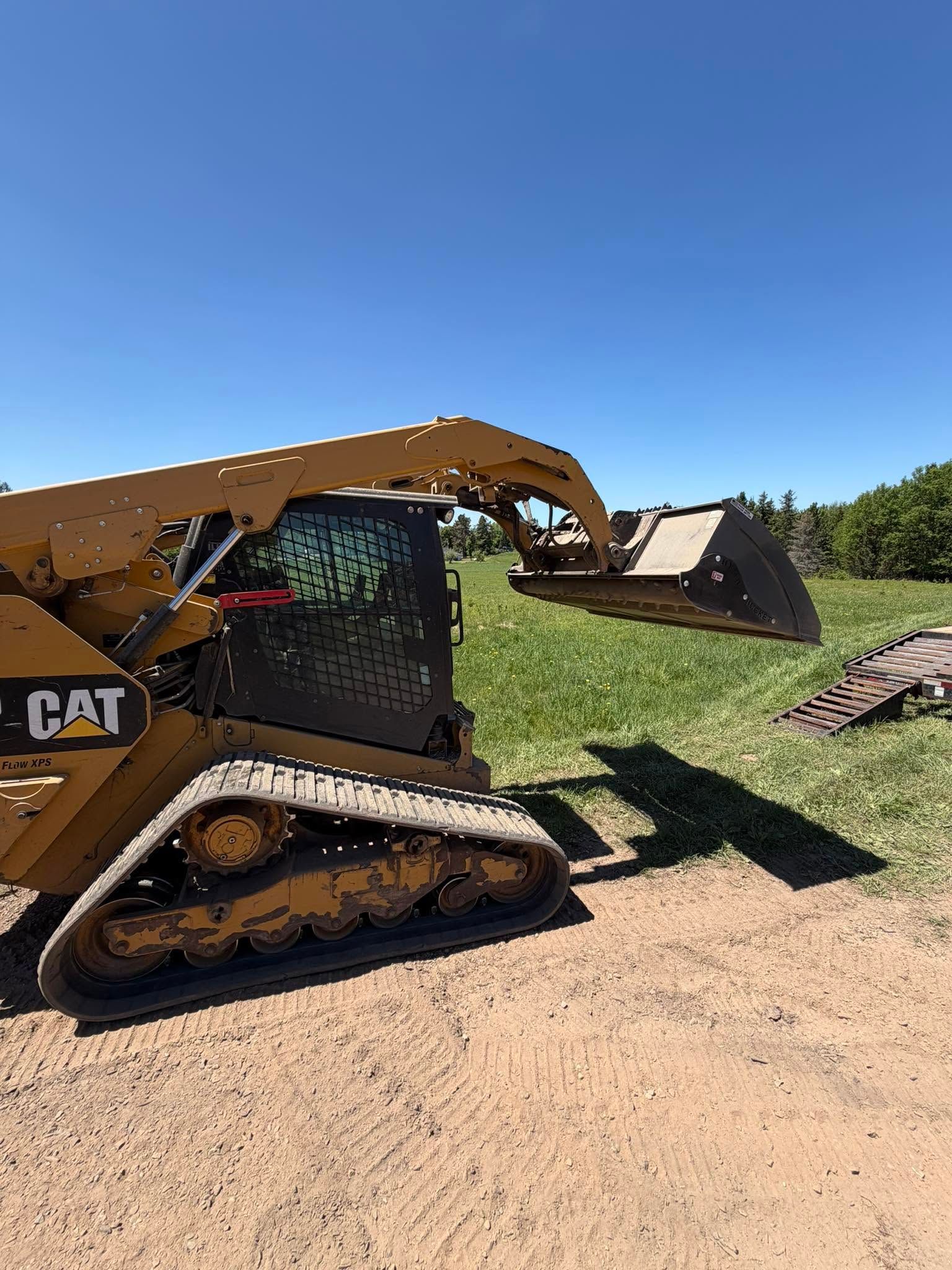 Yellow CAT skid steer loader dumping grass into a pile on a sunny farm field