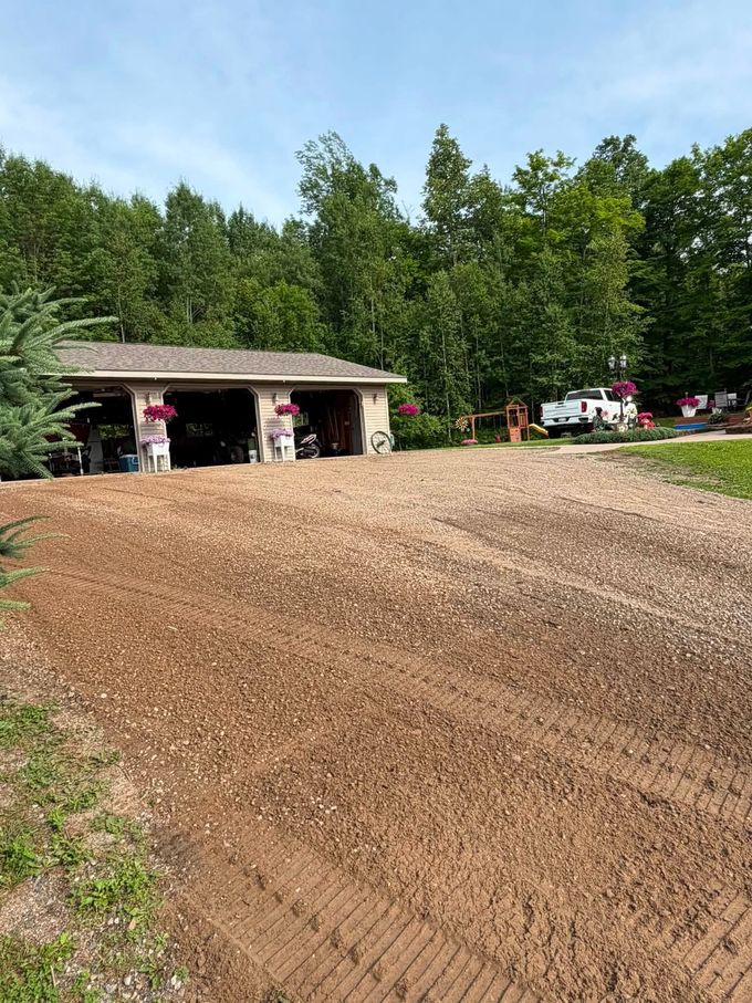 Gravel track at a wooded outdoor venue with people gathered under a small shelter in the background