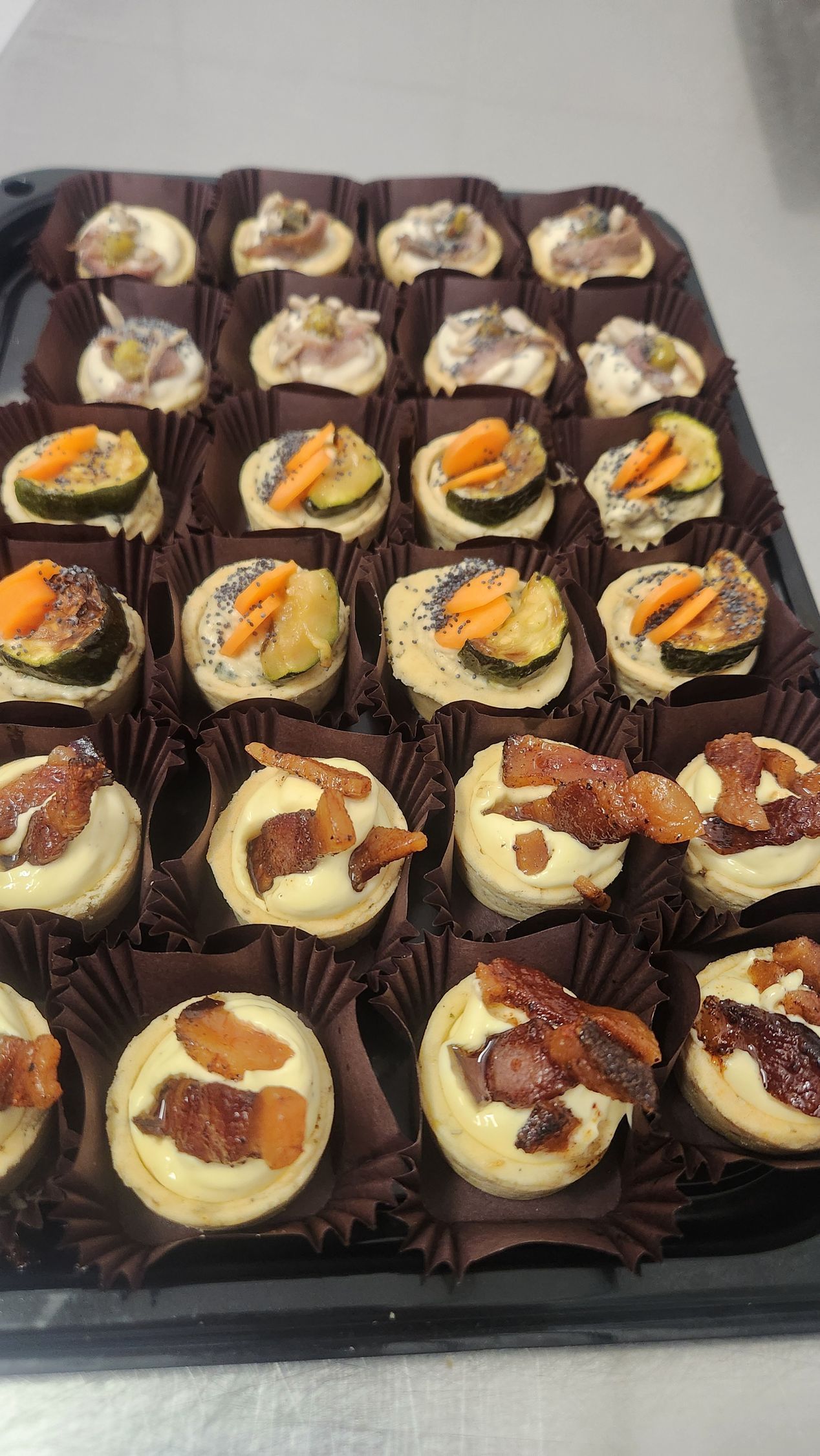 Vassoio di dessert assortiti in formato monoporzione con glassa bianca e guarnizione arancione, serviti in pirottini di carta marrone.