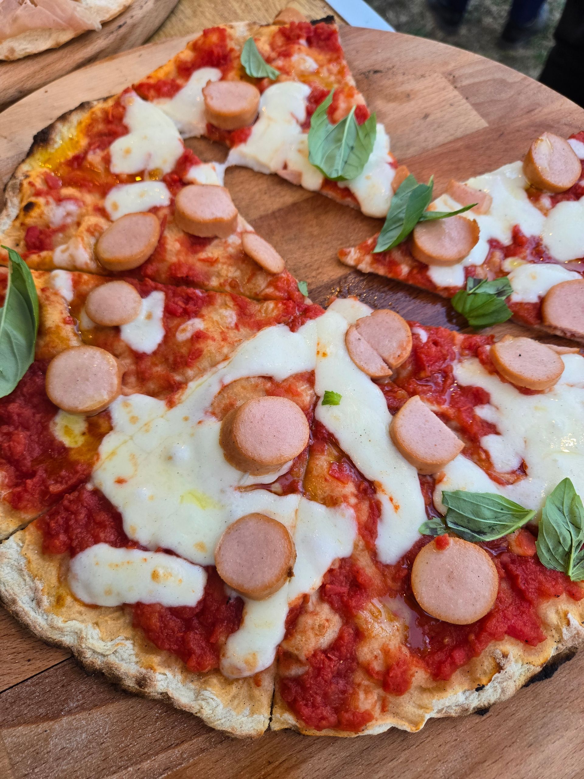 Pizza al salame piccante parzialmente mangiata con formaggio fuso e basilico su un tagliere di legno.
