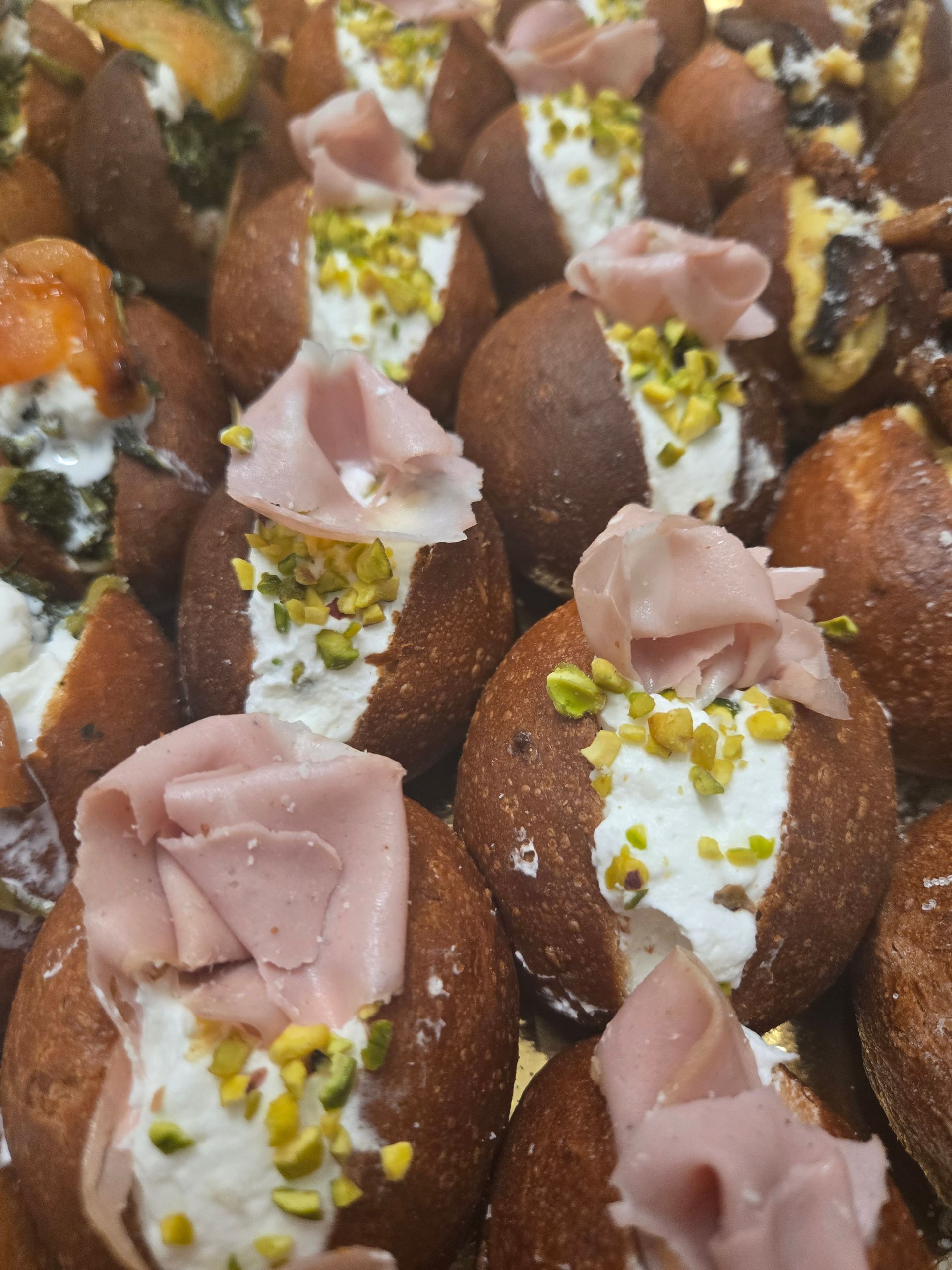 Pasticcini assortiti al cioccolato con glassa rosa e pistacchi tritati, disposti su un vassoio.