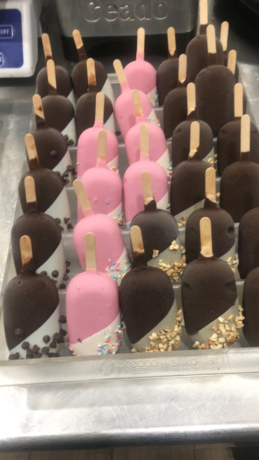 File di gelati su stecco ricoperti di cioccolato rosa e scuro in un banco frigo.