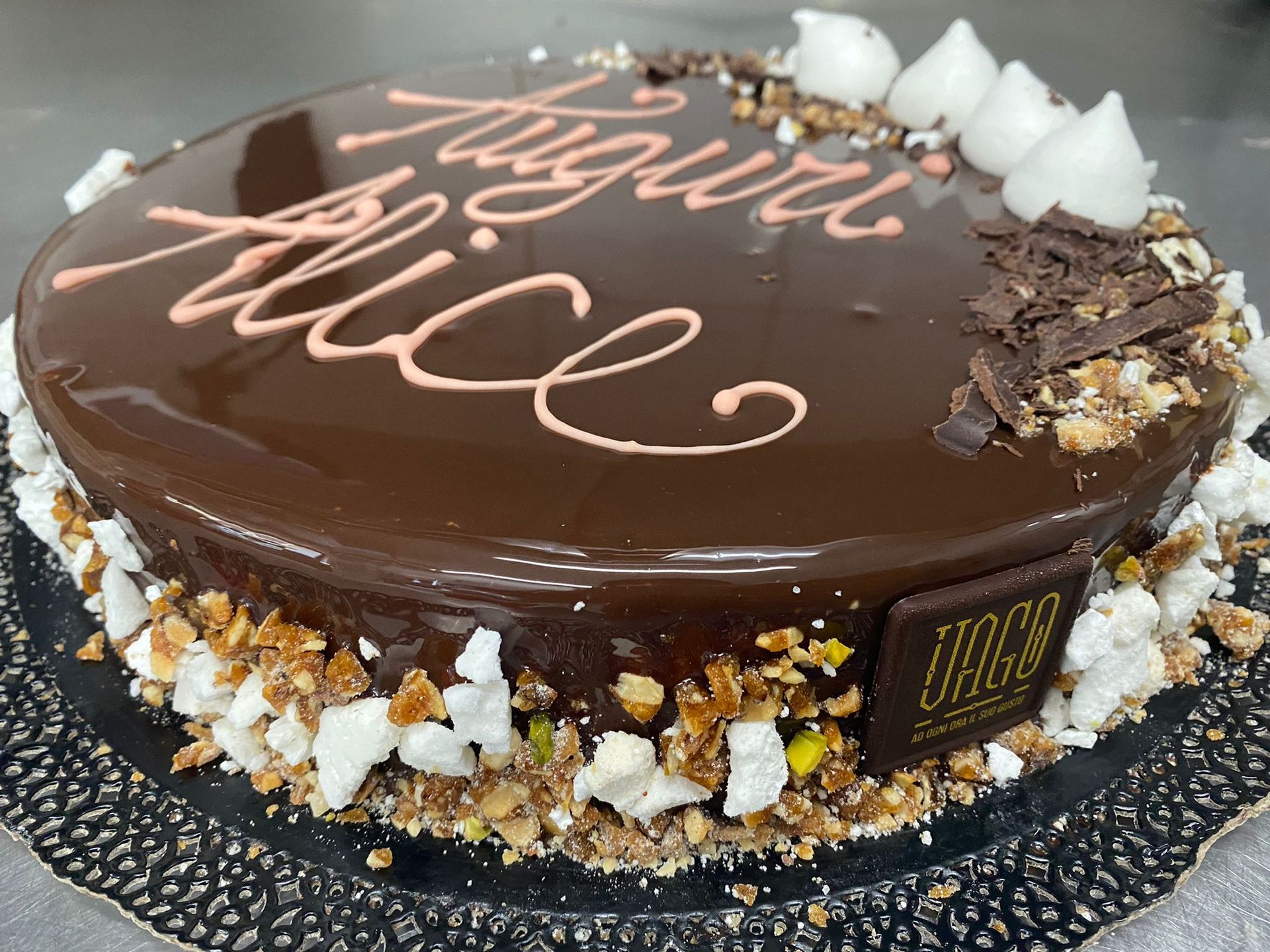 Torta al cioccolato con ganache lucida, bordo di cocco bianco e scritta in glassa rosa sulla parte superiore.