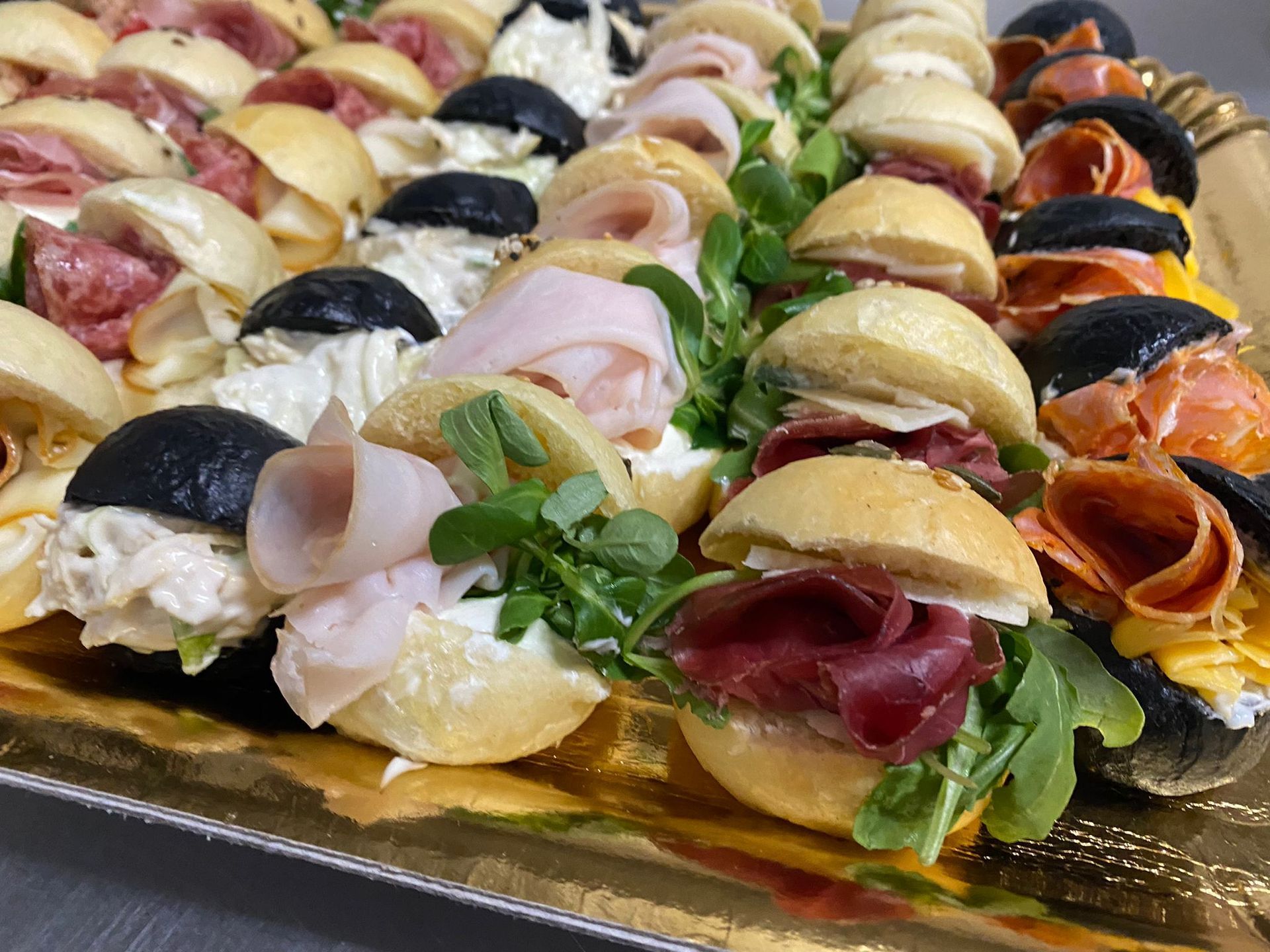 Assortimento di mini panini con salumi, verdure e pane, disposti su un vassoio.