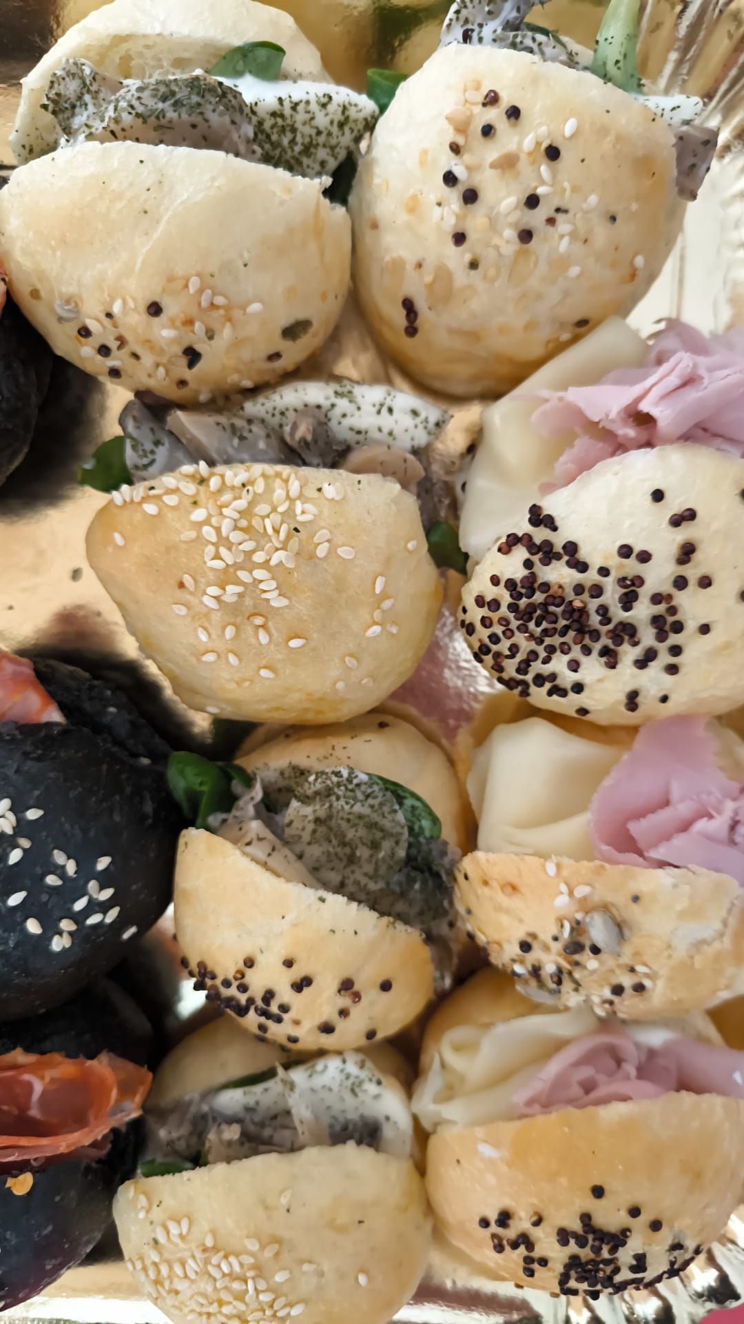 Un assortimento di panini e focaccine al sesamo con diversi condimenti, disposti su un vassoio.
