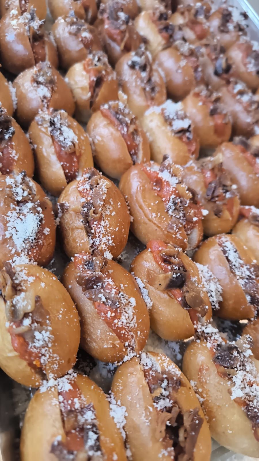 Decine di mini pasticcini ricoperti di zucchero a velo, disposti in file ordinate su un vassoio.