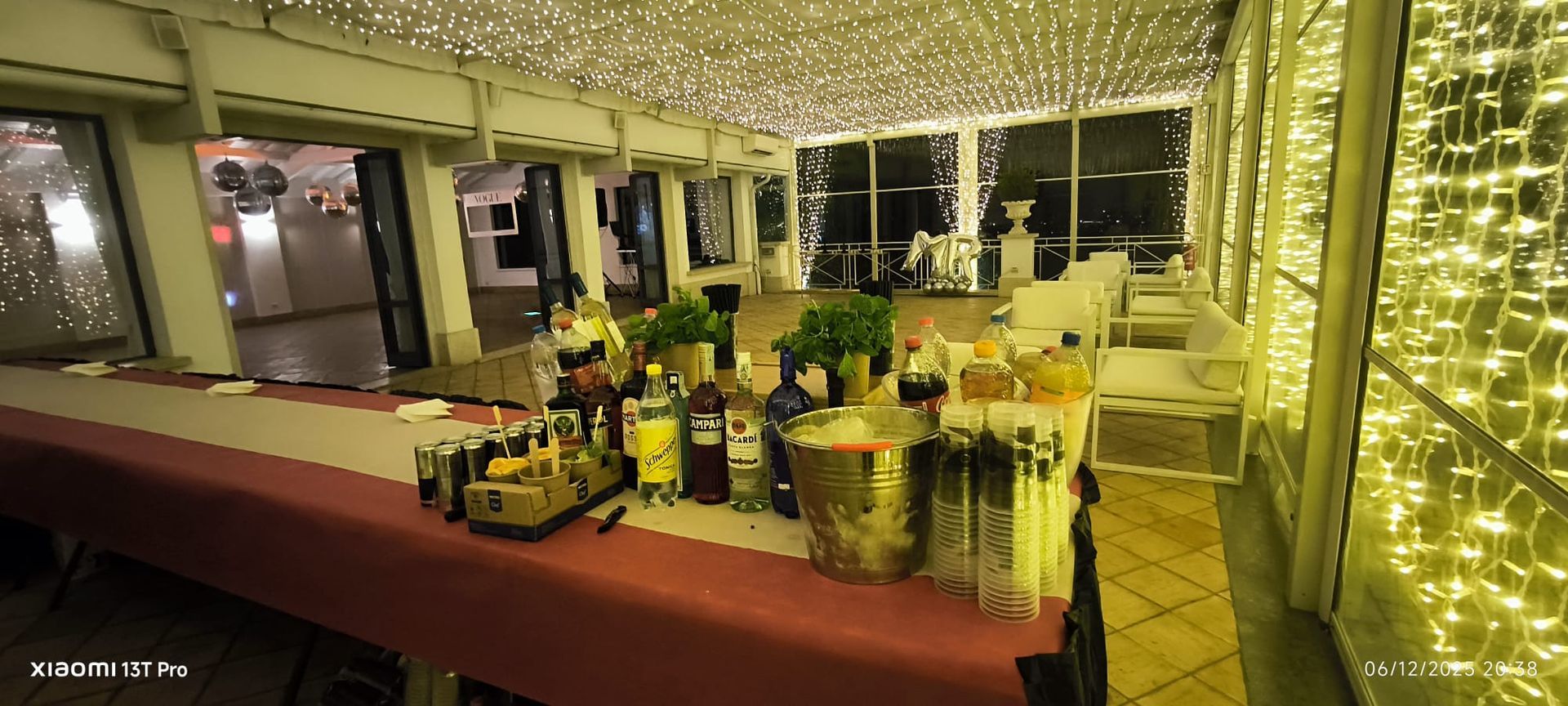 Tavolo da bar all'aperto illuminato d'oro con diverse bottiglie e bicchieri sotto un baldacchino di notte