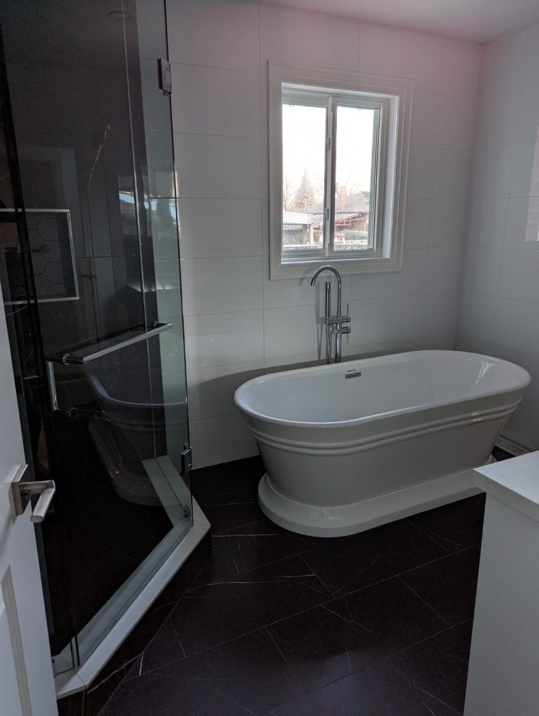 Modern bathroom with a freestanding tub, glass shower, and dark tile floor.