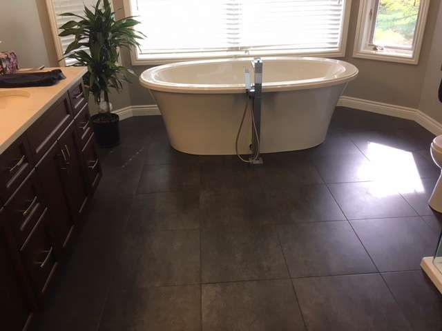 Bathroom with dark tiled floor, free-standing tub by a window, and dark wood vanity with a potted plant.