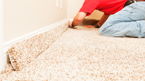 Person installing beige carpet in a room, kneeling at the baseboard.