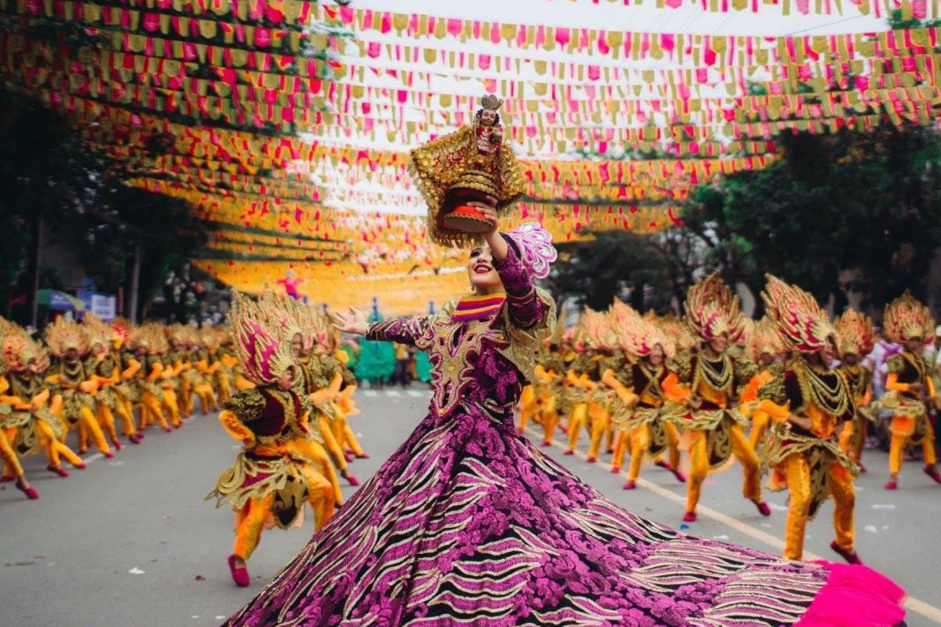 A woman in a long purple dress is dancing in a parade.