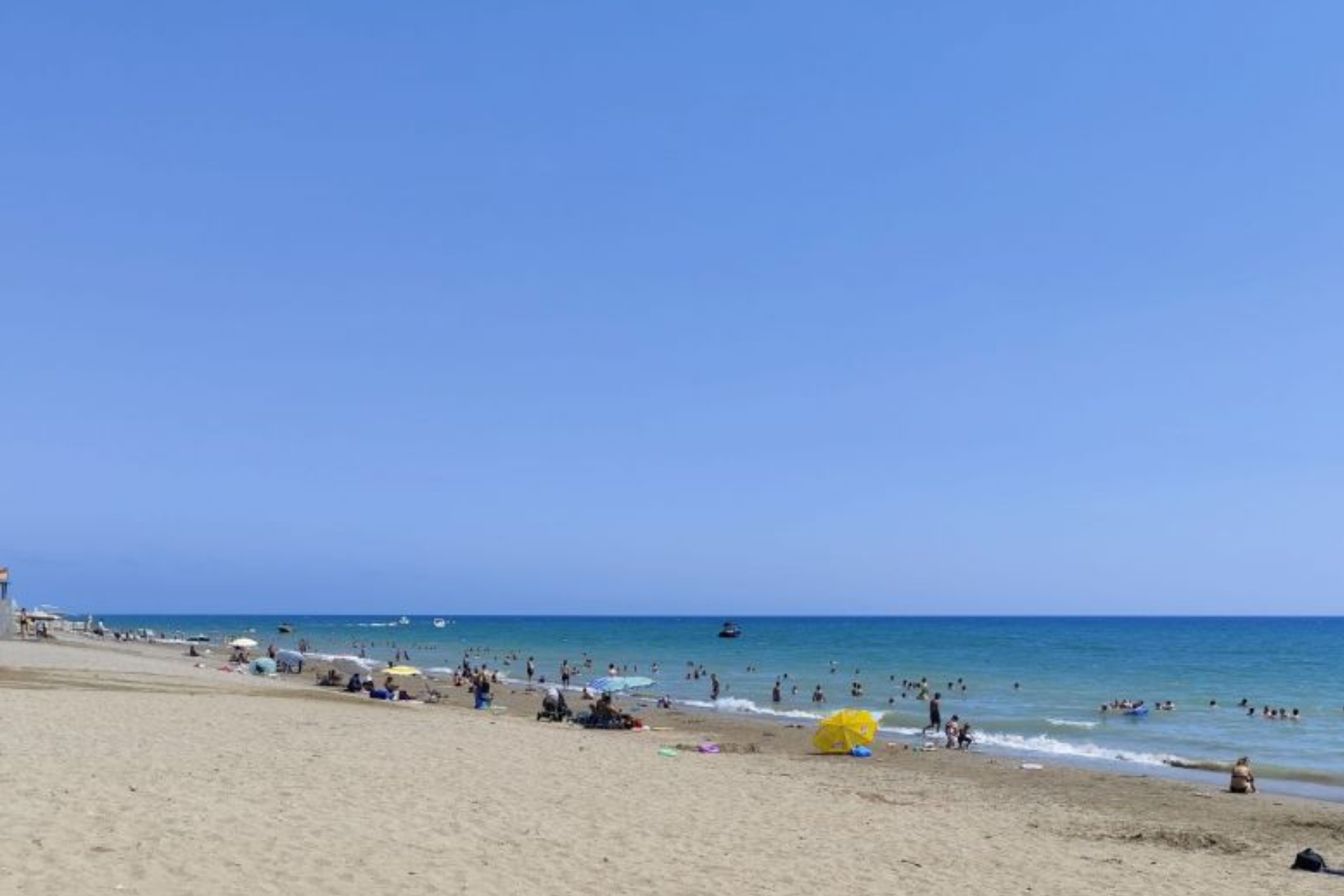 A beach filled with people and umbrellas on a sunny day.