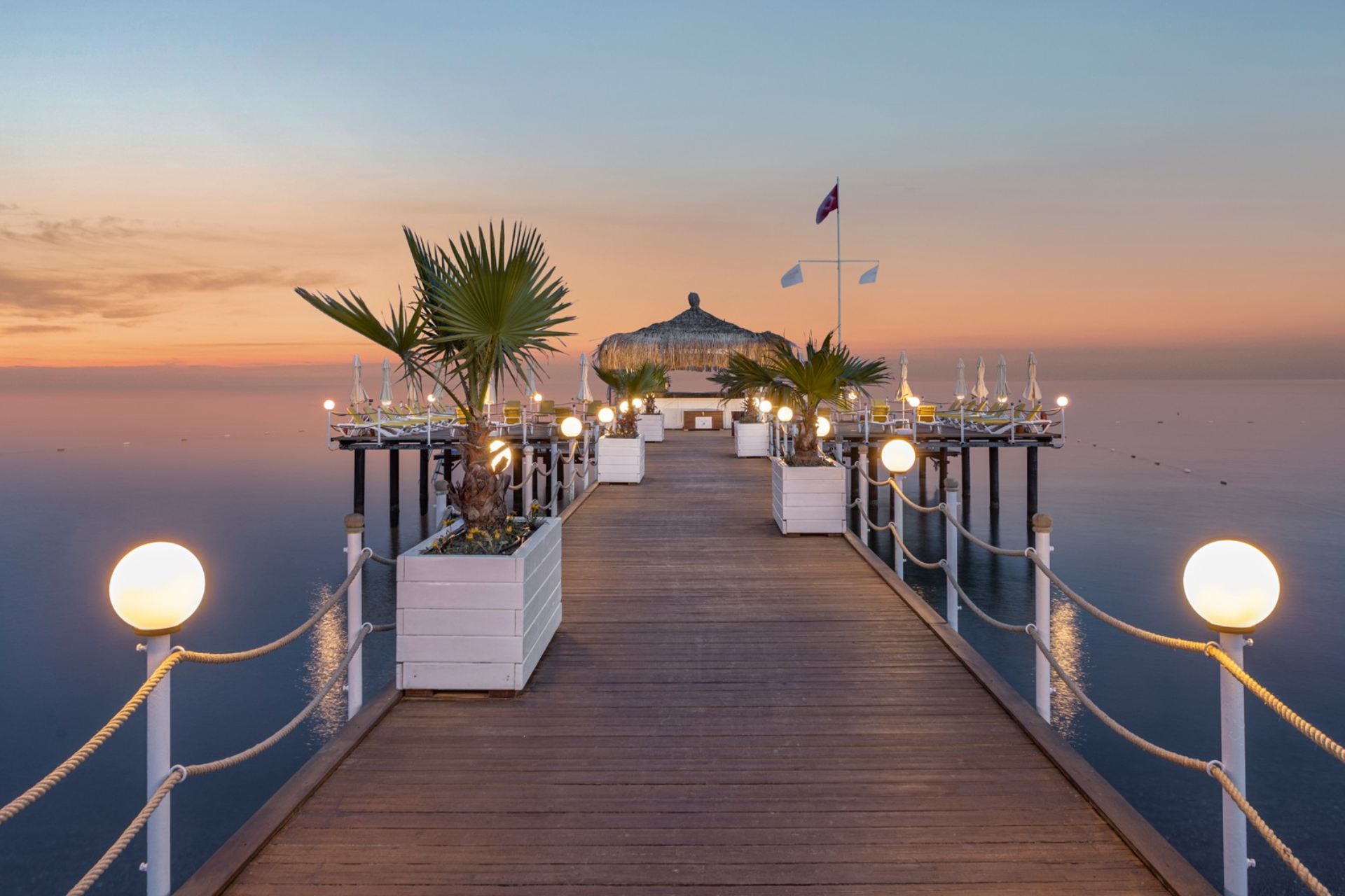 A wooden pier leading to a gazebo in the middle of the ocean at sunset.