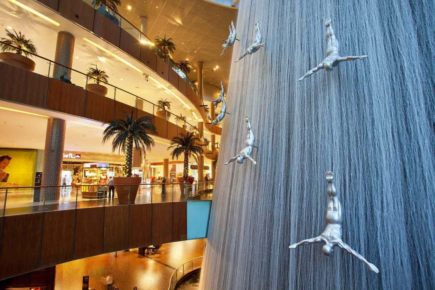 A waterfall in a shopping mall with sculptures of people hanging from it.