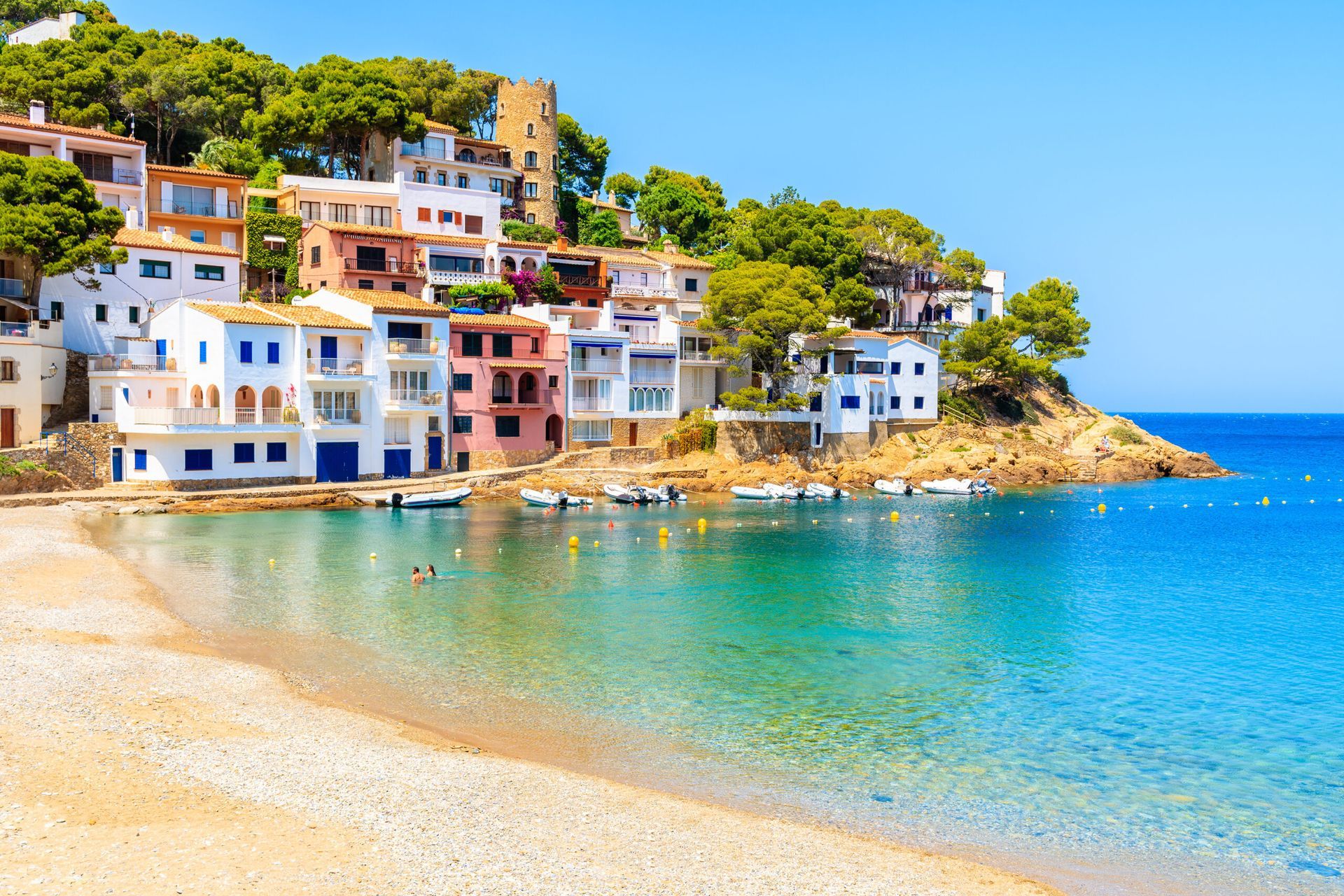 A beach with a small town in the background and boats in the water
