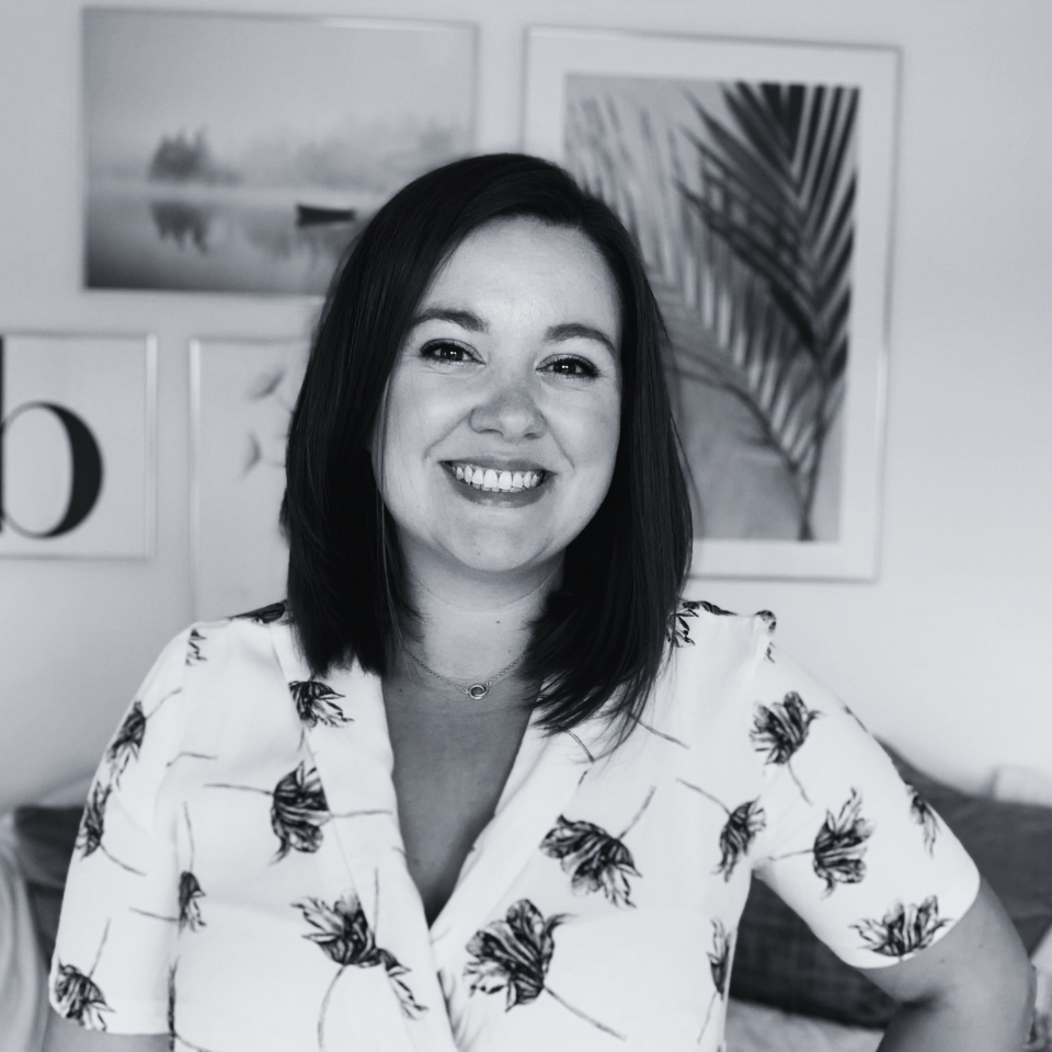 A woman in a floral shirt is smiling in a black and white photo.