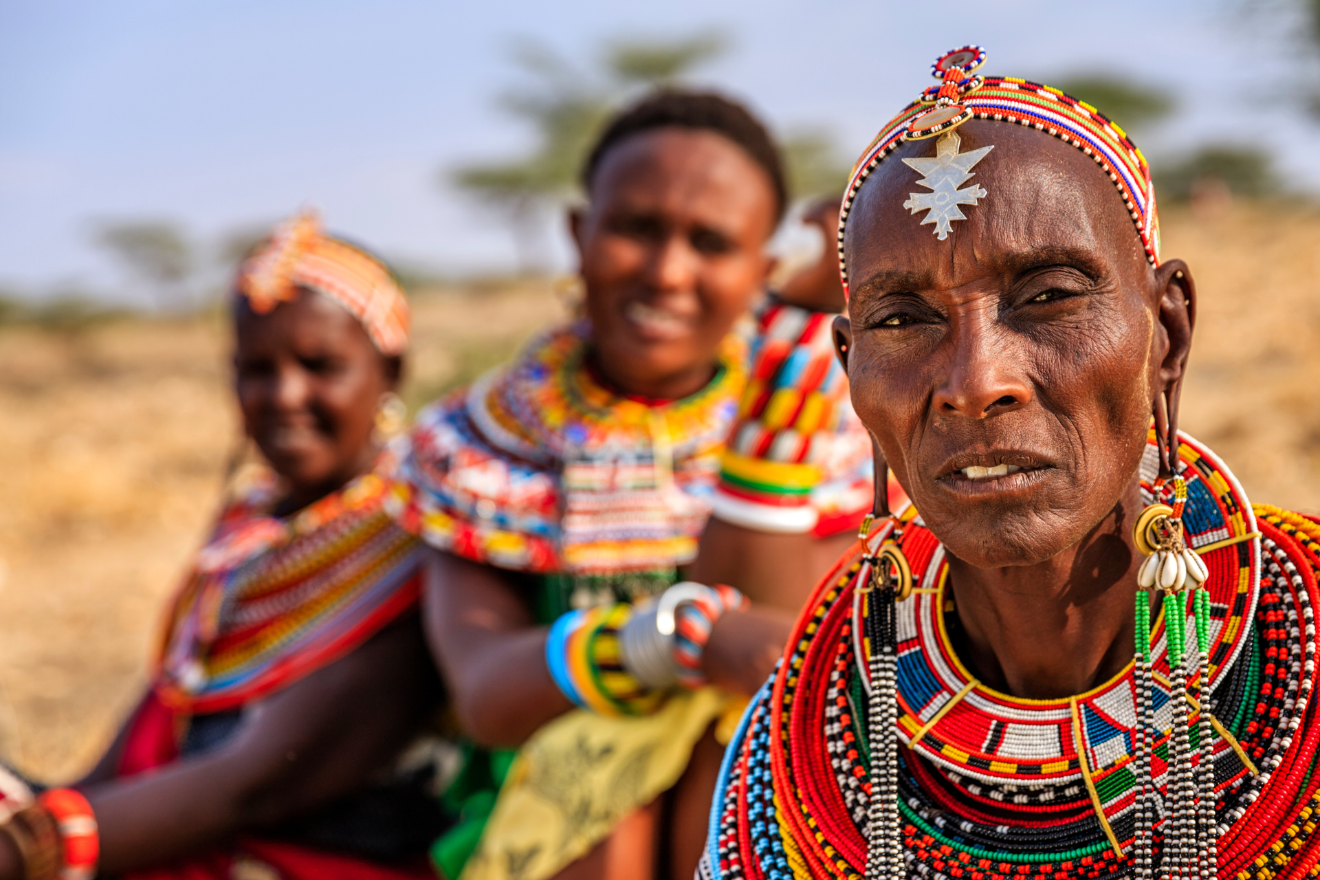 A group of african women wearing colorful necklaces and earrings are posing for a picture.