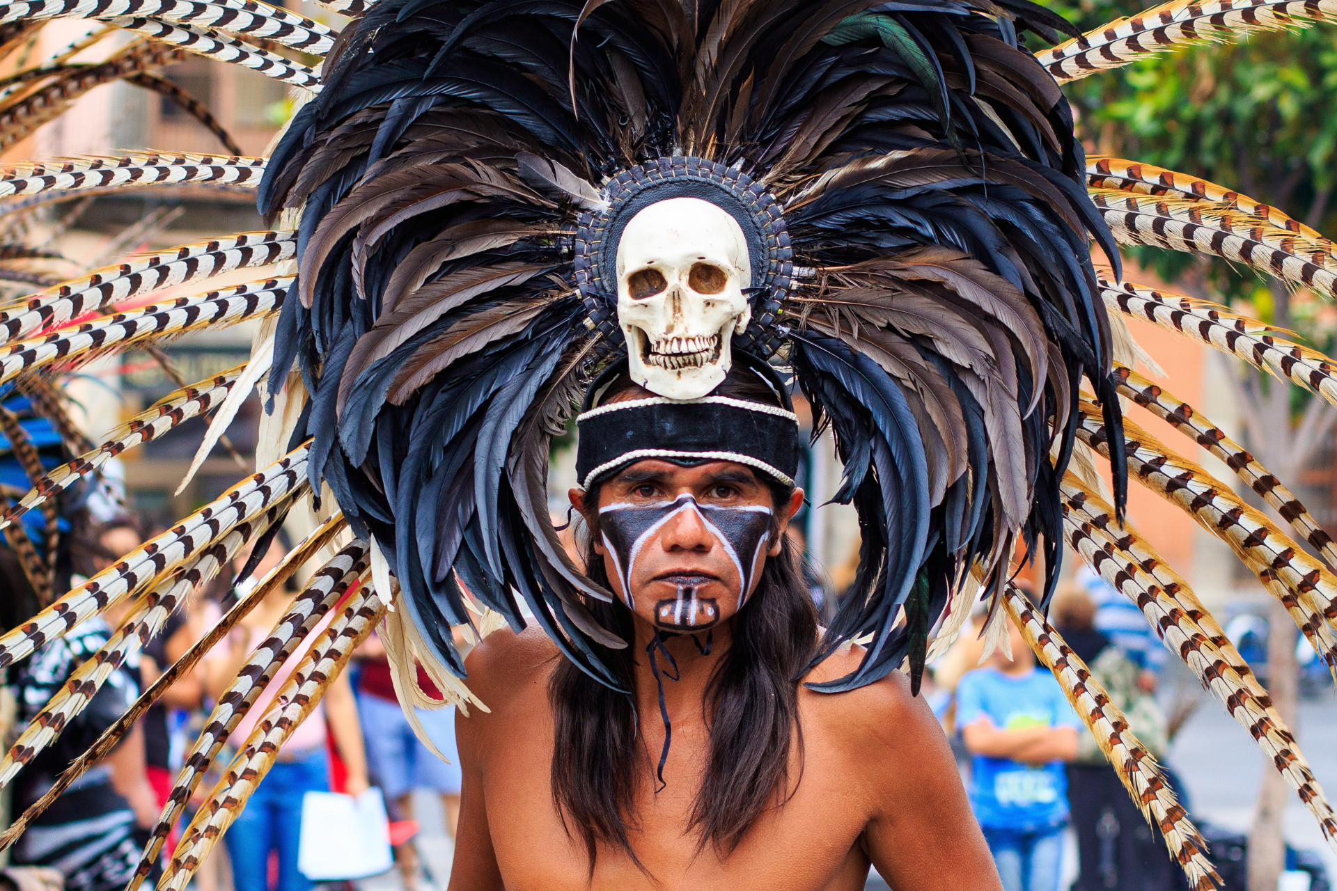 A man is wearing a feathered headdress with a skull on it.