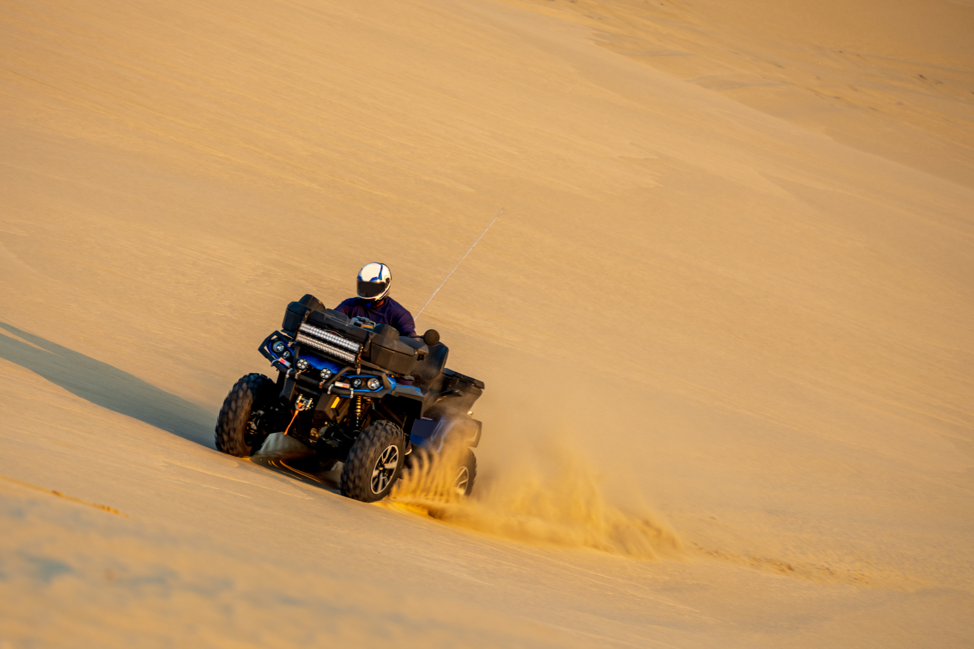 A person is riding an atv down a sand dune.