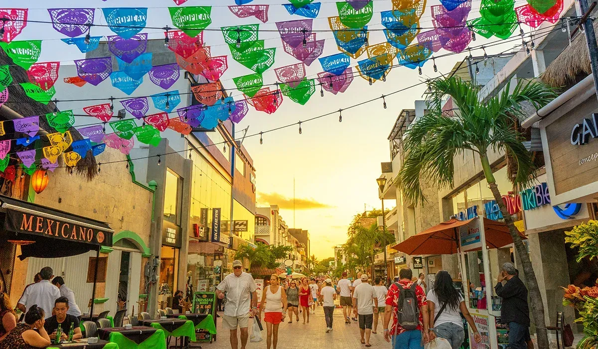 A crowd of people are walking down a street with colorful umbrellas hanging from the ceiling.