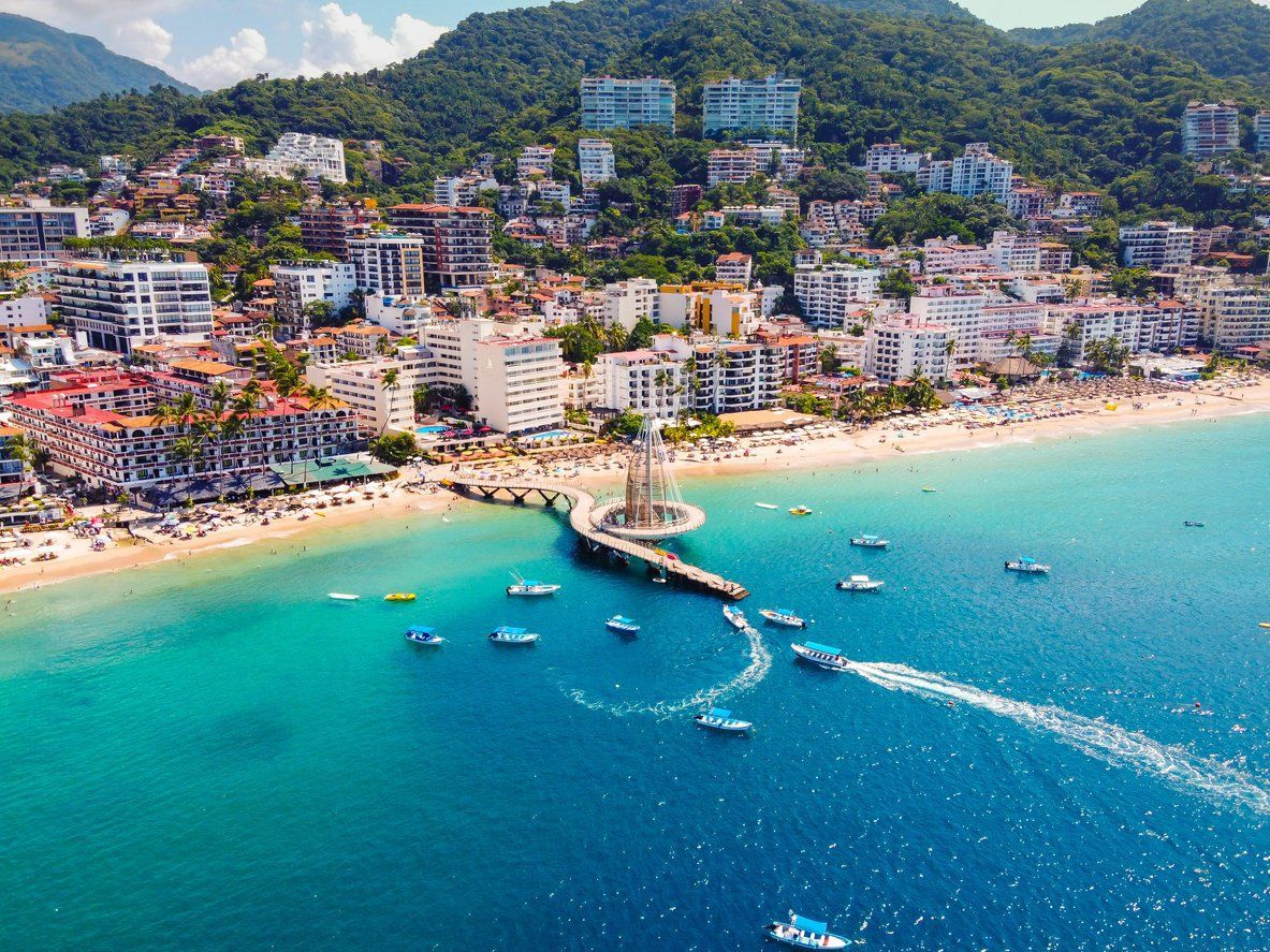 An aerial view of a beach with boats in the water and a city in the background.