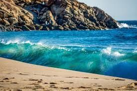 A beach with waves crashing on the shore and a rocky cliff in the background.