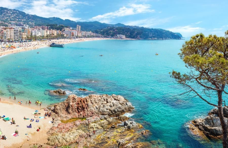 A beach with a boat in the water and a city in the background.