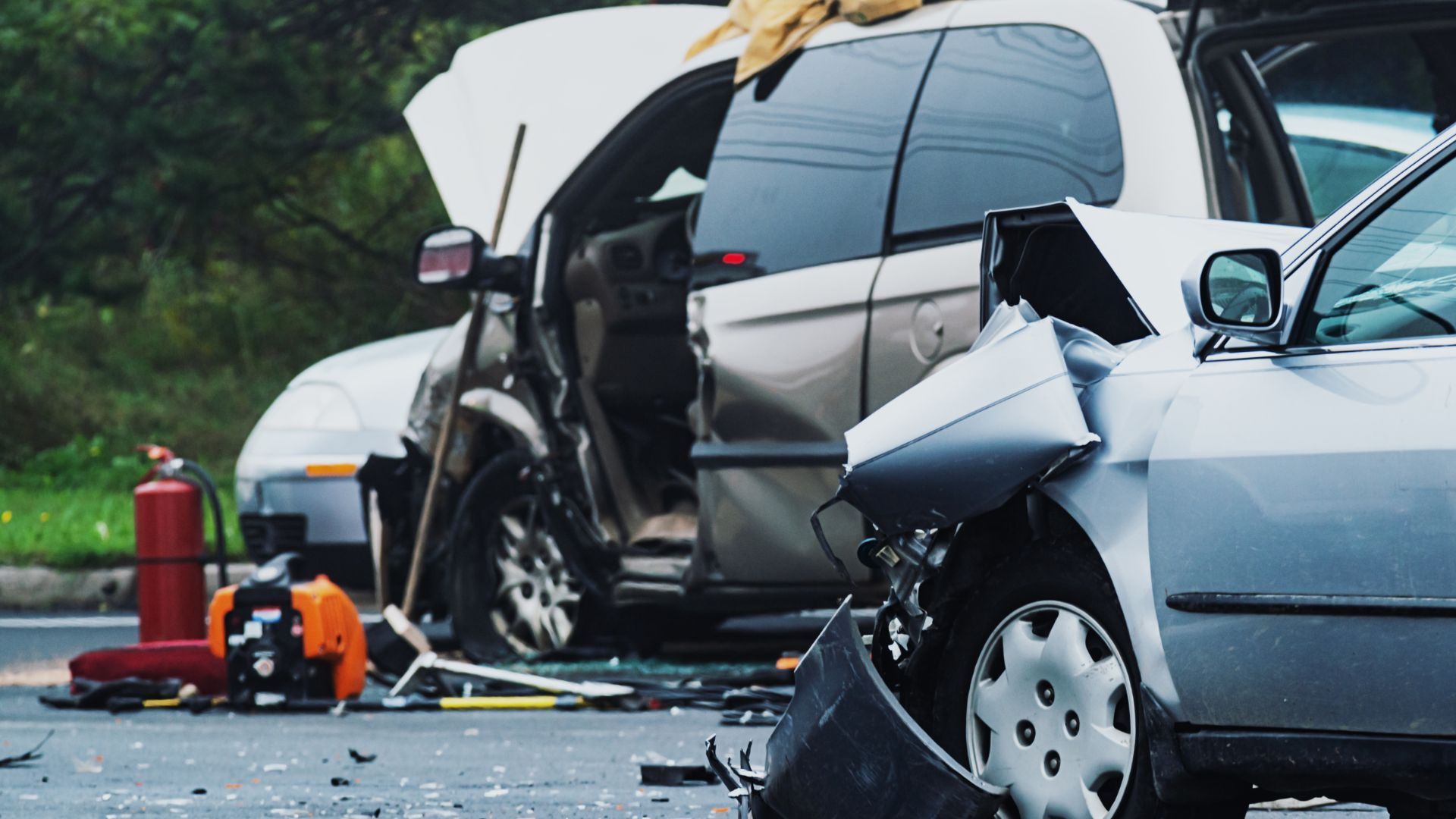 Severe car crash with two damaged vehicles, debris on the road, and emergency equipment nearby