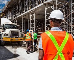 Construction workers in orange safety vests and hard hats near concrete trucks at a building site