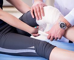 Trainer wrapping a knee with white bandage during sports injury treatment