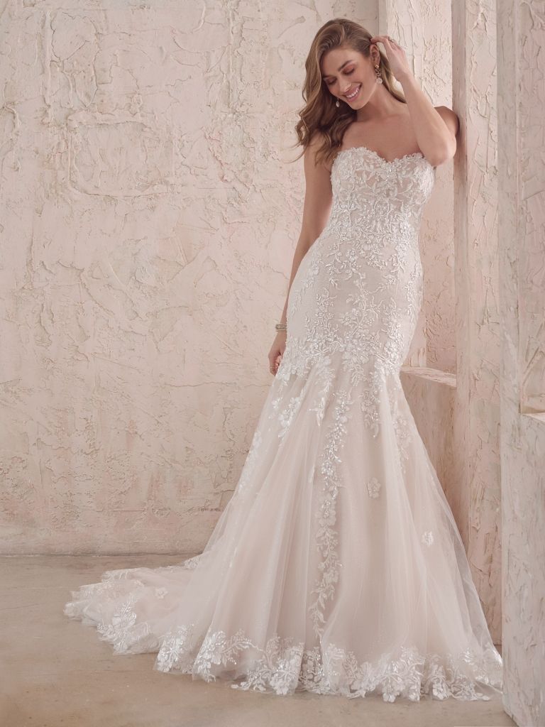 A woman in a white wedding dress is standing in front of a wall.