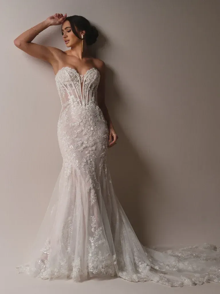 A woman in a white wedding dress is standing in front of a wall.