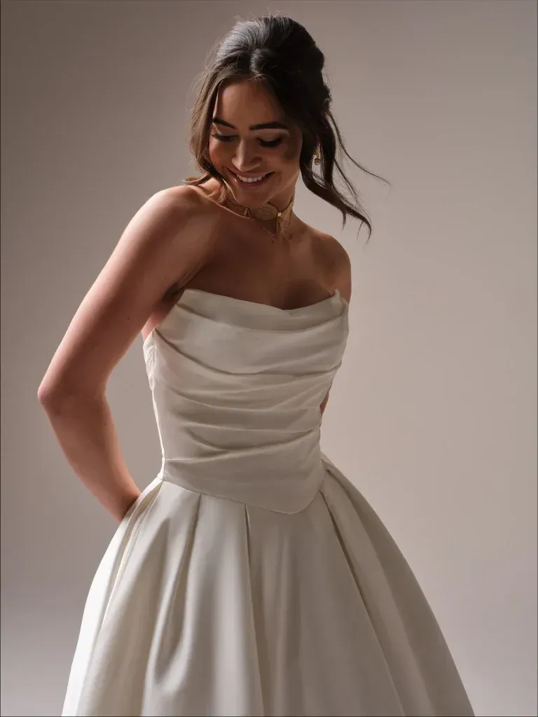 A woman in a white wedding dress is smiling and looking down.