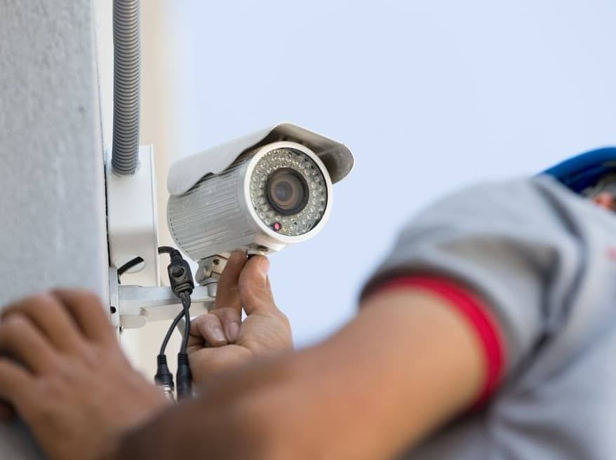 A Man Is Installing A Security Camera On The Side Of A Building — Advanced Alarms Mackay Pty Ltd In South Mackay, QLD
