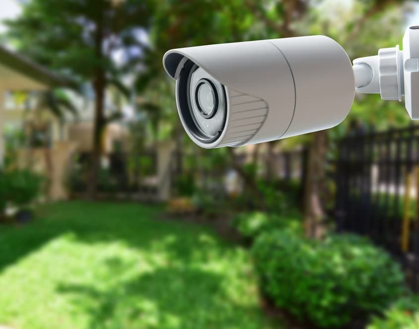 A Security Camera Is Hanging From A Fence In A Backyard — Advanced Alarms Mackay Pty Ltd In South Mackay, QLD