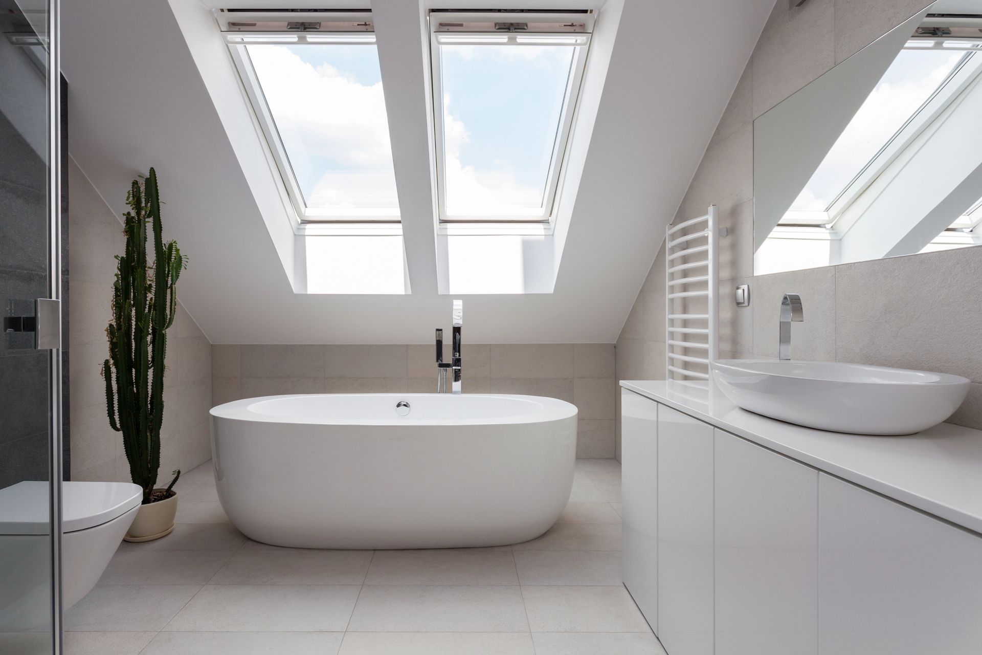 Modern white bathroom with skylights, freestanding tub, double sinks, and a potted plant