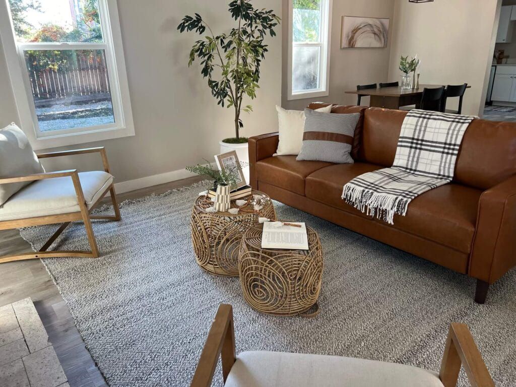 Living room with brown leather sofa, rug, wicker coffee tables, and wood chairs.