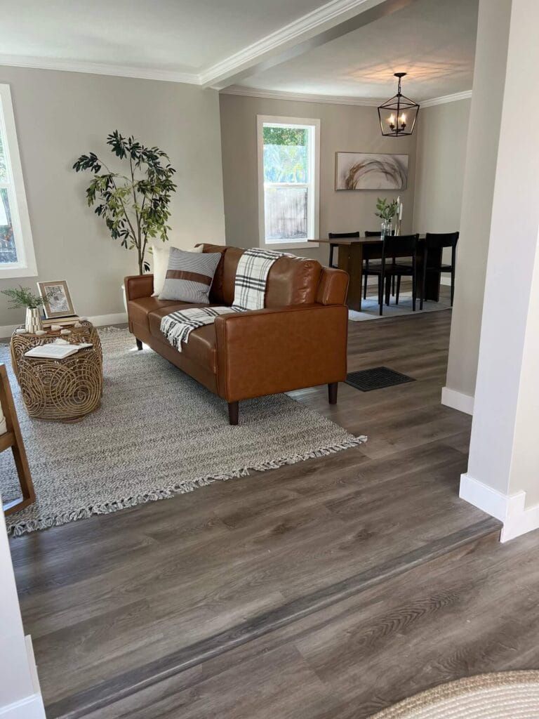 Living room with brown leather sofa, rug, and dining area in the background.