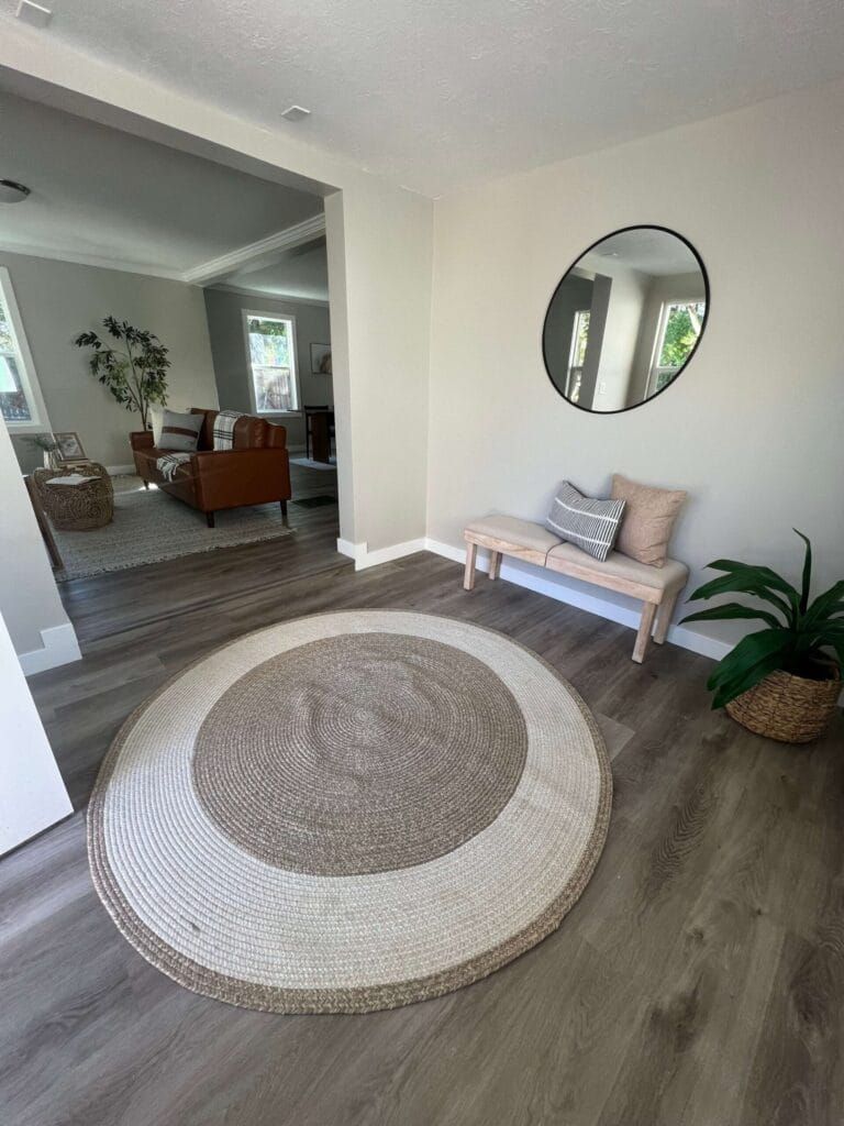 Entryway with a round jute rug, bench, mirror, and potted plant.