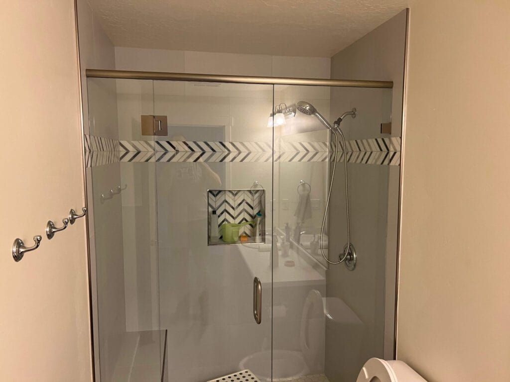 Shower with glass doors, silver fixtures, a decorative band, and a built-in shelf.