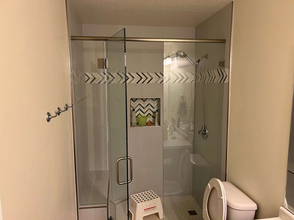 Bathroom with glass shower door, toilet, and small step stool. Beige walls and decorative etched glass.