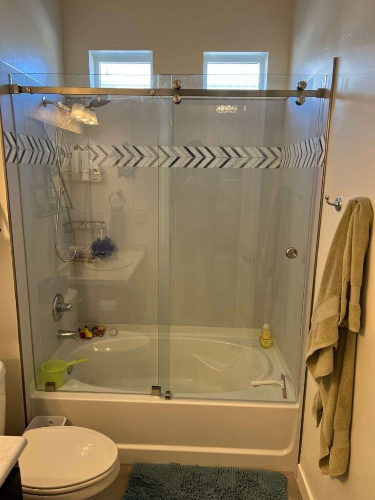 Bathroom with a glass shower door and a bathtub. The shower door has a decorative arrow pattern. A towel hangs on the wall.